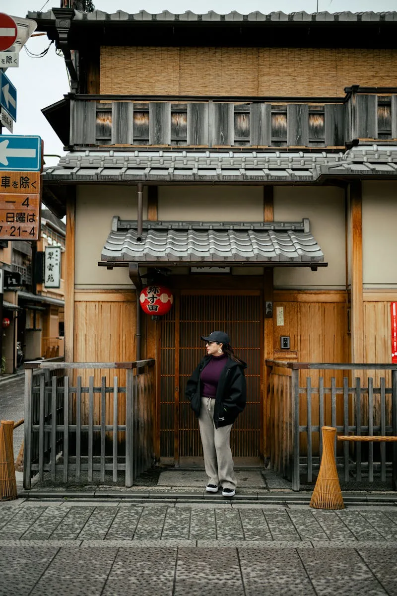 Person standing beside a traditional wooden Japanese building on a street. Captured during the day.